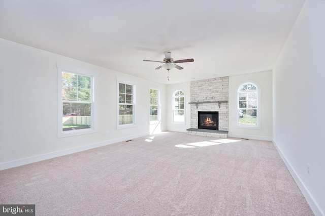 unfurnished living room with ceiling fan, a stone fireplace, and light carpet