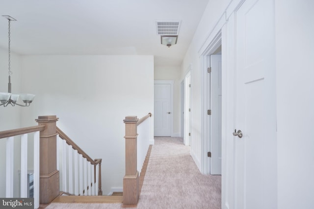 hall featuring light carpet and an inviting chandelier