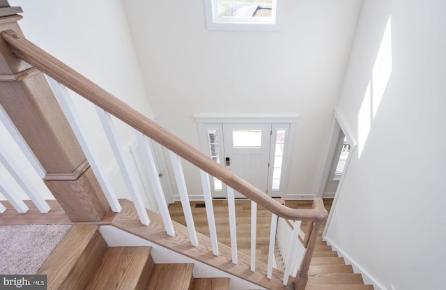 stairs with hardwood / wood-style flooring, a towering ceiling, and a healthy amount of sunlight