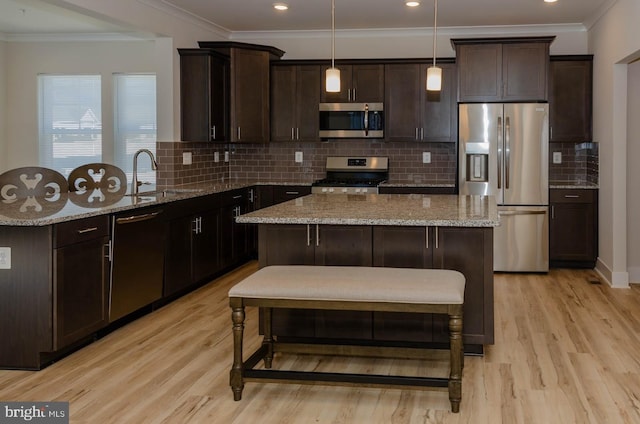 kitchen featuring appliances with stainless steel finishes, pendant lighting, sink, light stone counters, and light hardwood / wood-style flooring