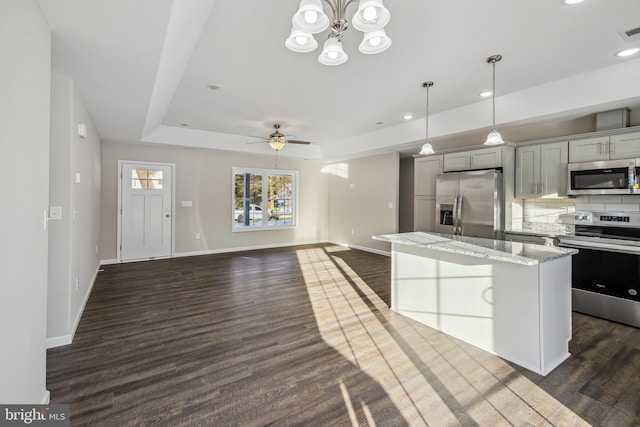 kitchen with appliances with stainless steel finishes, a kitchen island, decorative backsplash, gray cabinets, and a raised ceiling