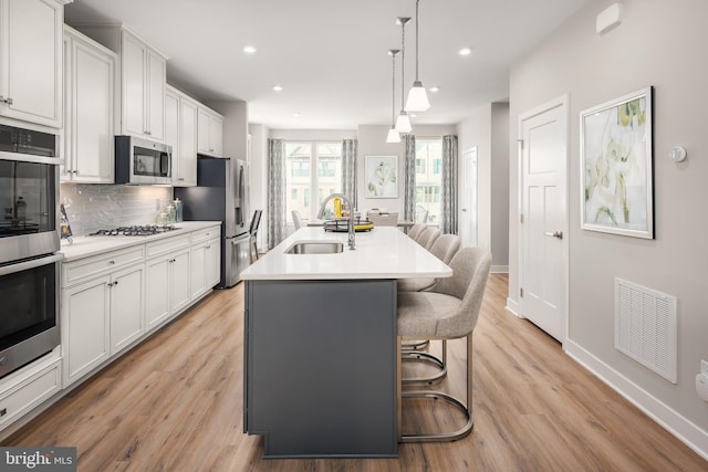 kitchen featuring a kitchen bar, stainless steel appliances, a kitchen island with sink, pendant lighting, and white cabinets