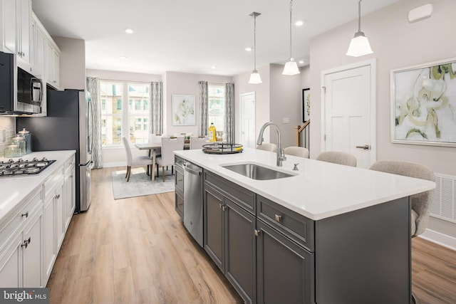 kitchen featuring an island with sink, stainless steel appliances, hanging light fixtures, white cabinets, and sink