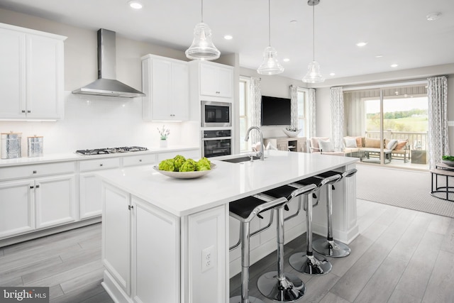 kitchen with wall chimney exhaust hood, an island with sink, sink, stainless steel gas stovetop, and built in microwave