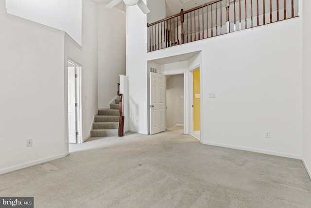 unfurnished living room with a towering ceiling, light colored carpet, and ceiling fan