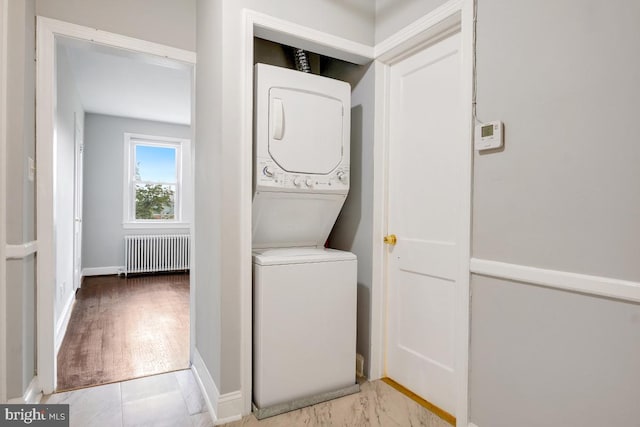 laundry area with stacked washer / dryer and radiator heating unit