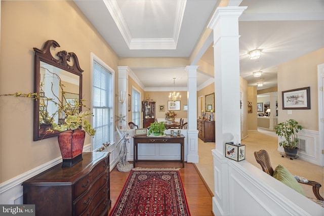 hall with ornate columns, crown molding, a chandelier, light wood-type flooring, and a tray ceiling