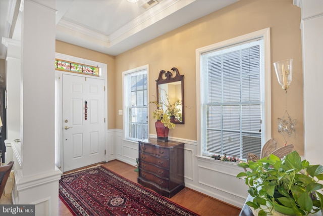 entrance foyer with ornamental molding, light hardwood / wood-style floors, and a tray ceiling