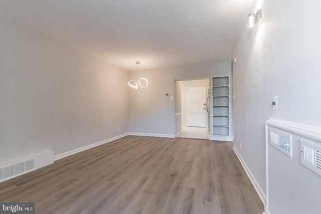 empty room featuring light wood-type flooring and a notable chandelier