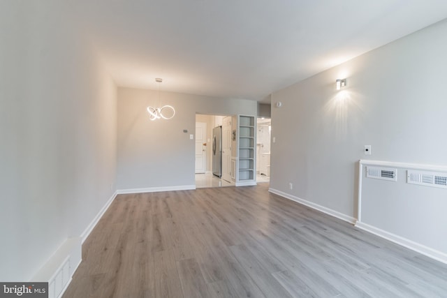 spare room featuring light wood-type flooring and an inviting chandelier