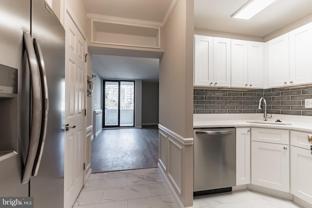 kitchen featuring backsplash, sink, appliances with stainless steel finishes, ornamental molding, and white cabinets