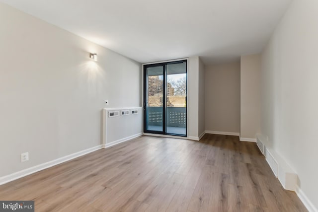 empty room featuring floor to ceiling windows and light hardwood / wood-style flooring