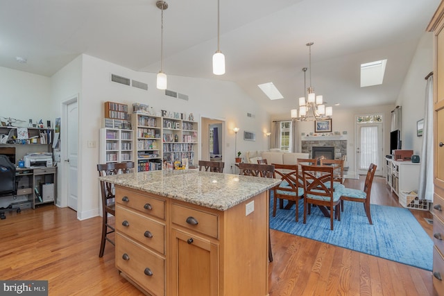 kitchen with decorative light fixtures, a fireplace, light stone countertops, light hardwood / wood-style flooring, and a center island