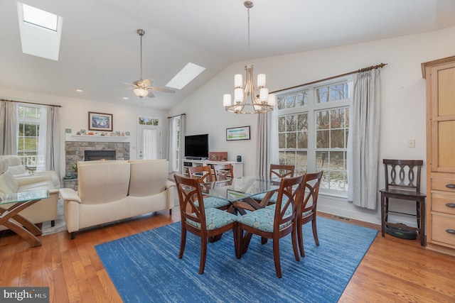 dining room with ceiling fan with notable chandelier, hardwood / wood-style floors, vaulted ceiling, and a fireplace