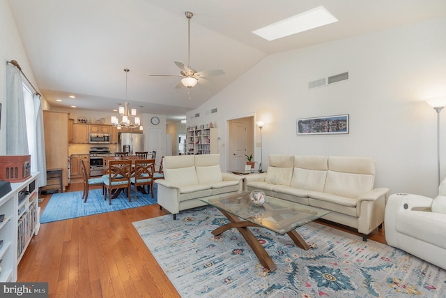 living room featuring light hardwood / wood-style floors, vaulted ceiling with skylight, and ceiling fan with notable chandelier