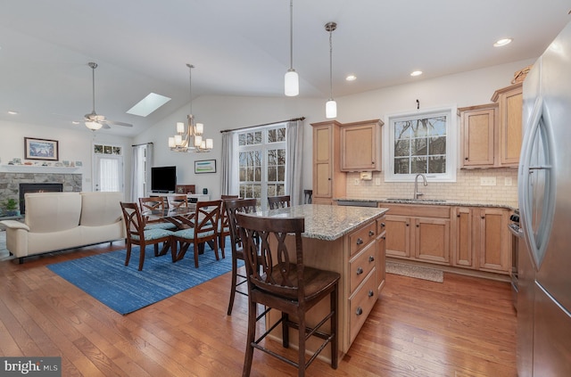 kitchen with ceiling fan with notable chandelier, light stone countertops, a kitchen island, sink, and backsplash