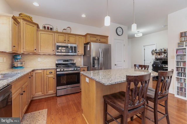 kitchen featuring hardwood / wood-style floors, appliances with stainless steel finishes, a center island, decorative light fixtures, and backsplash