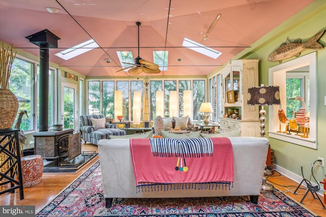 sunroom featuring ceiling fan, a wood stove, vaulted ceiling with skylight, and a healthy amount of sunlight