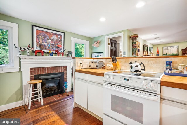 kitchen featuring backsplash, a brick fireplace, electric range, white cabinetry, and wood counters