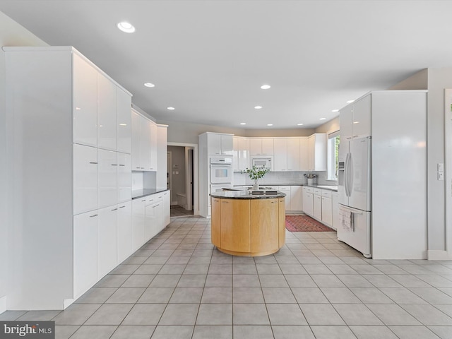 kitchen with light tile patterned floors, white cabinetry, white appliances, and a center island