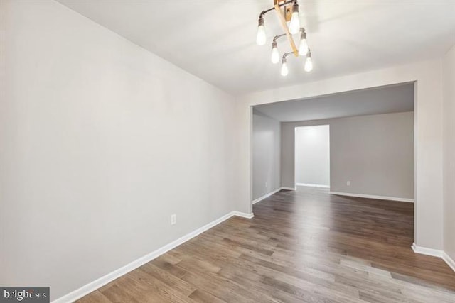 empty room featuring wood-type flooring and a chandelier