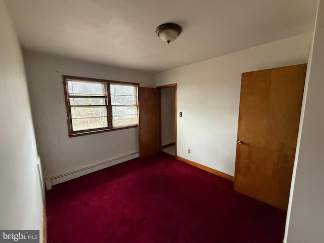 empty room featuring a baseboard heating unit and dark colored carpet