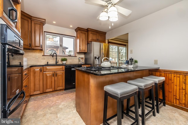 kitchen featuring sink, tasteful backsplash, dark stone countertops, a kitchen breakfast bar, and black appliances