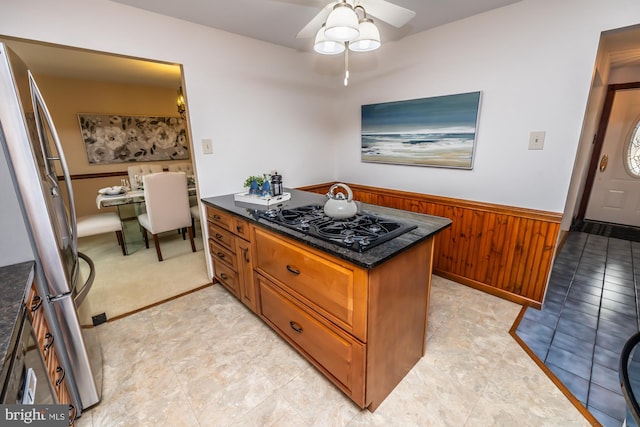 kitchen featuring wooden walls, stainless steel refrigerator, black gas cooktop, dark stone countertops, and ceiling fan