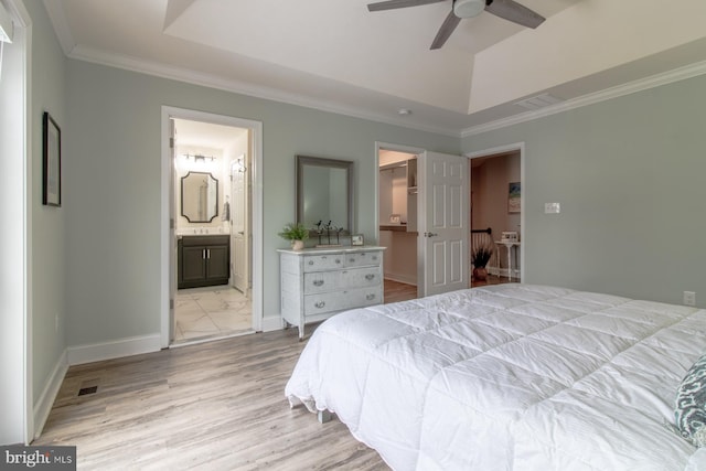 bedroom with ceiling fan, ensuite bath, a tray ceiling, and a spacious closet