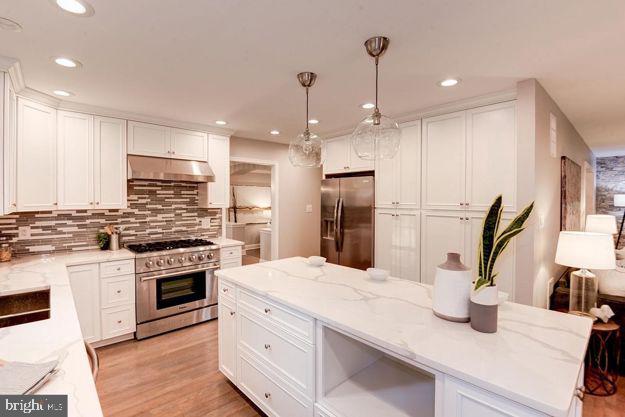 kitchen with light stone countertops, pendant lighting, white cabinets, appliances with stainless steel finishes, and backsplash