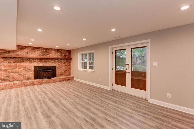 unfurnished living room with light hardwood / wood-style floors, a wood stove, brick wall, and french doors