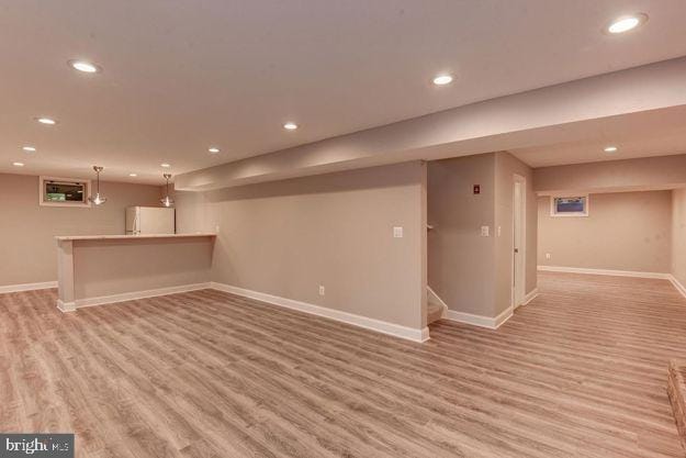 basement with white refrigerator and light hardwood / wood-style flooring