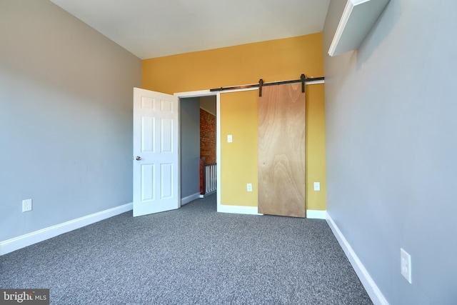 unfurnished bedroom with dark colored carpet and a barn door