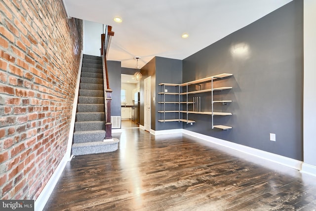 unfurnished living room with brick wall, dark hardwood / wood-style flooring, and a notable chandelier