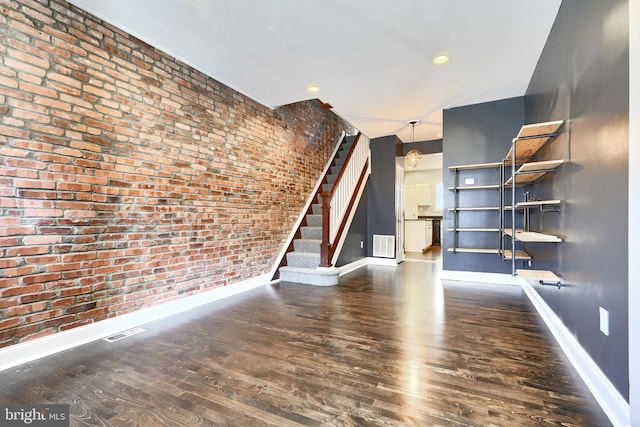 unfurnished living room featuring brick wall and dark hardwood / wood-style flooring