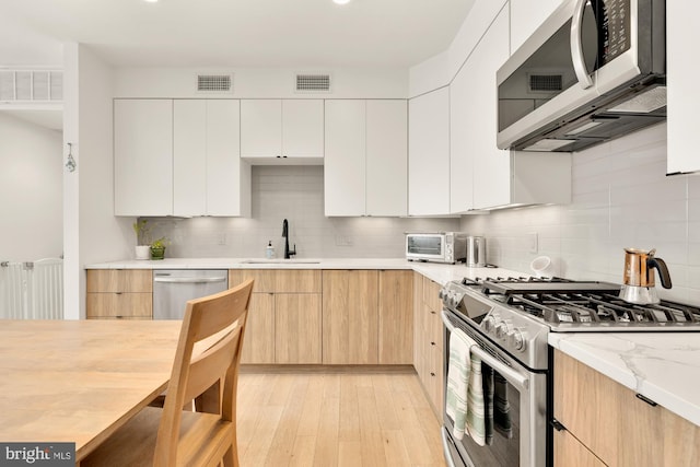 kitchen featuring appliances with stainless steel finishes, backsplash, white cabinetry, and sink