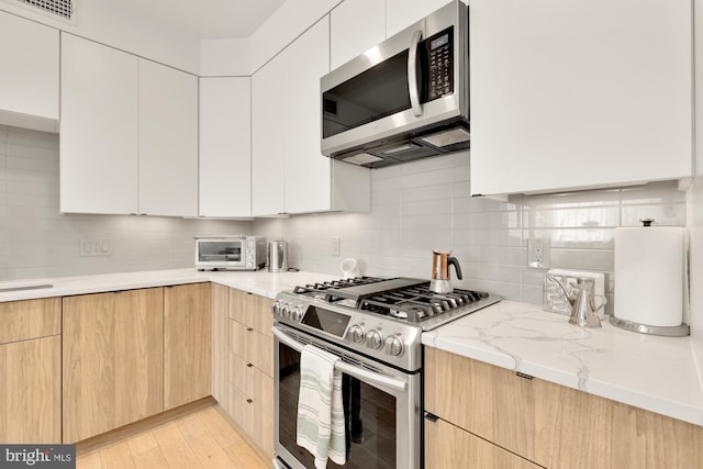 kitchen featuring white cabinetry, appliances with stainless steel finishes, tasteful backsplash, light brown cabinetry, and light stone counters