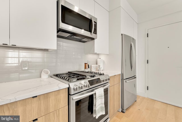 kitchen with white cabinetry, stainless steel appliances, backsplash, light stone counters, and light hardwood / wood-style flooring