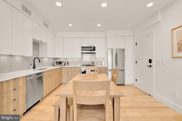 kitchen with appliances with stainless steel finishes, light hardwood / wood-style floors, backsplash, and white cabinetry