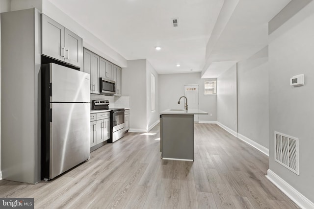 kitchen with a kitchen island with sink, gray cabinets, stainless steel appliances, and light hardwood / wood-style floors