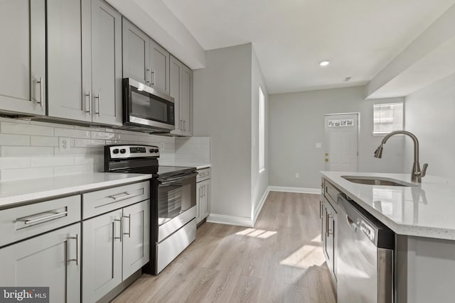 kitchen featuring sink, decorative backsplash, stainless steel appliances, light stone countertops, and light wood-type flooring