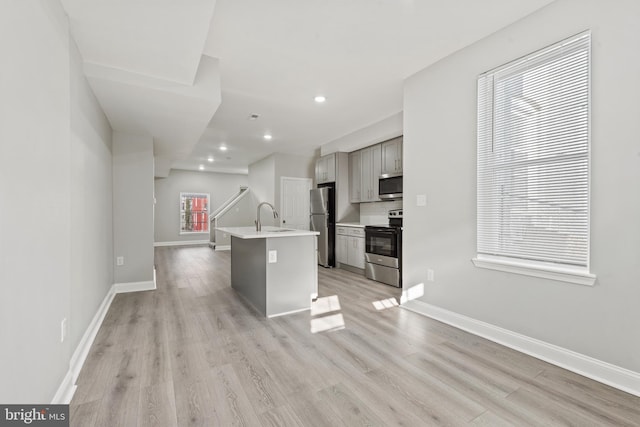 kitchen featuring a kitchen island with sink, gray cabinets, light hardwood / wood-style flooring, and appliances with stainless steel finishes