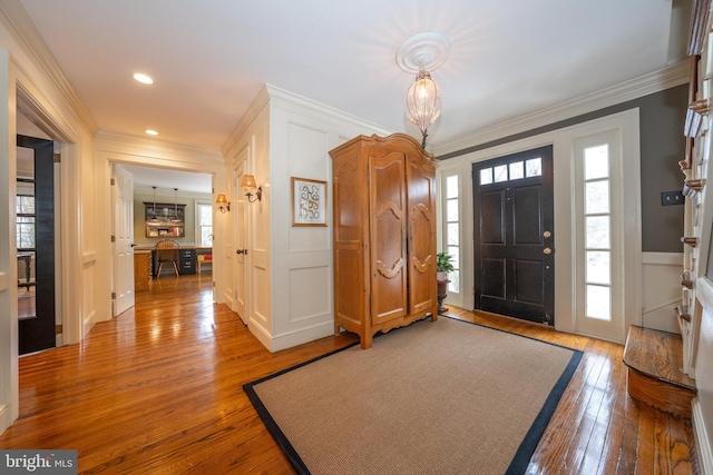 entrance foyer featuring crown molding, a healthy amount of sunlight, and wood-type flooring