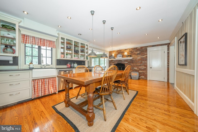 dining room with brick wall, a fireplace, ornamental molding, light hardwood / wood-style flooring, and sink