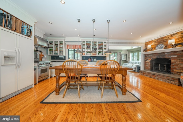 dining area featuring a fireplace, ornamental molding, and light hardwood / wood-style flooring