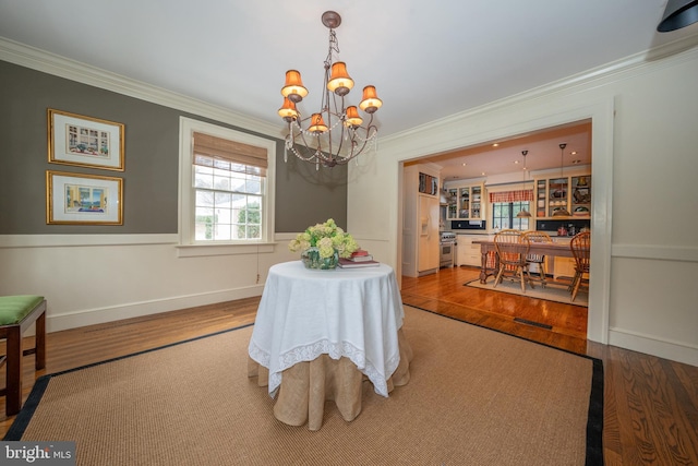 dining space with crown molding, wood-type flooring, plenty of natural light, and a notable chandelier