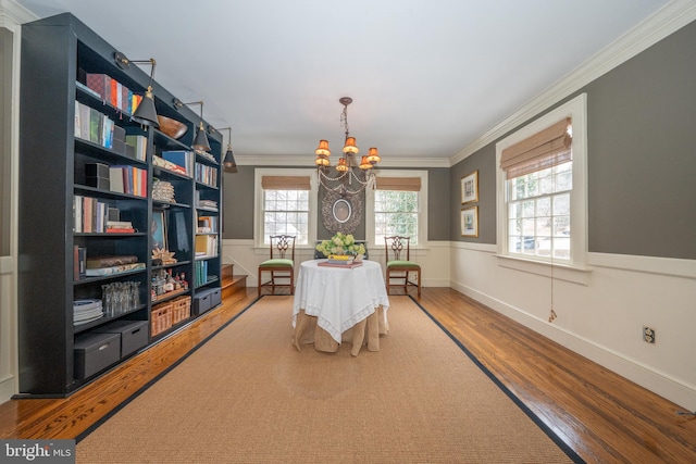 dining area with wood-type flooring, ornamental molding, and a chandelier