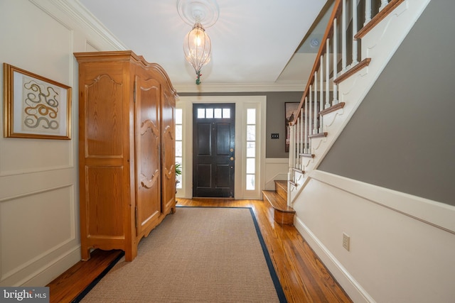 entryway with crown molding, light hardwood / wood-style floors, and a notable chandelier