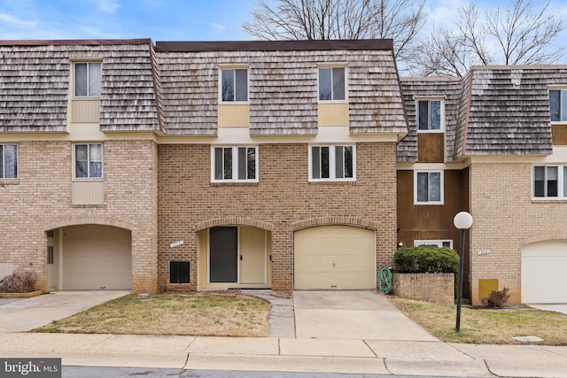 townhome / multi-family property featuring driveway, a garage, mansard roof, and brick siding