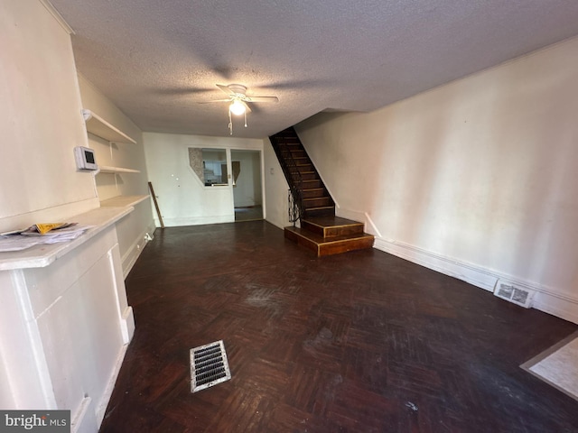 unfurnished living room with ceiling fan, a textured ceiling, and dark parquet flooring